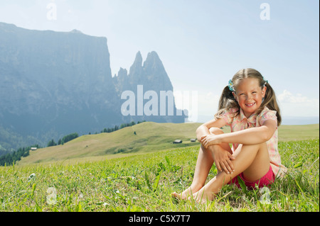 Italy, South Tyrol, Seiseralm, Girl (6-7) sitting in meadow Stock Photo