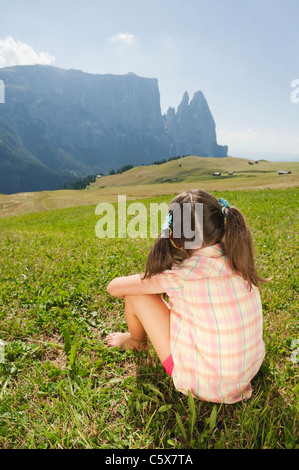 Italy, South Tyrol, Seiseralm, Girl (6-7) sitting in meadow, rear view Stock Photo