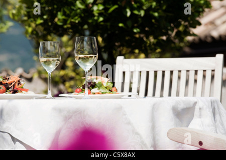 Italy, South Tyrol, Laid table, with mixed salad on plates and two glasses with white wine