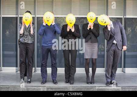 Germany, Hamburg, Five Business people standing in front of office building, hiding faces behind balloons Stock Photo