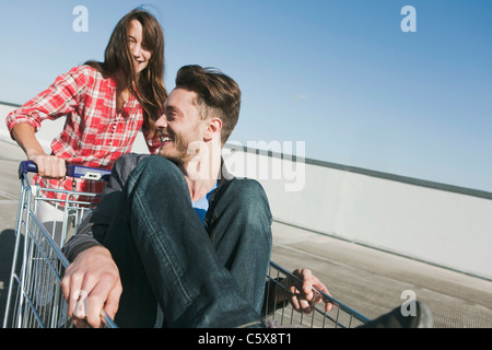 Germany, Berlin, Young woman pushing young man in shopping cart Stock Photo