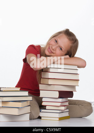 Girl sitting besides stack of books against white background, smiling , portrait Stock Photo