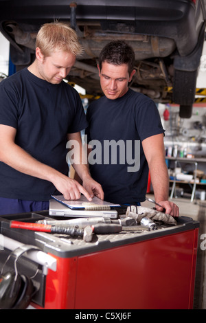 A pair of mechanics working on a car looking a service order Stock Photo