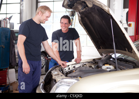 Two mechanics looking at and working on a car in a repair shop Stock Photo