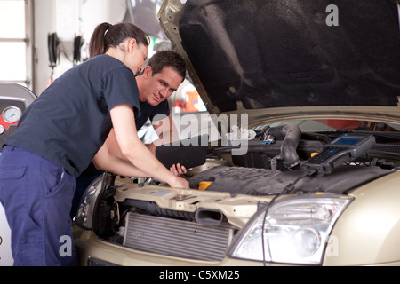Man and woman team of mechanics using digital tablet while diagnosing car engine. Stock Photo