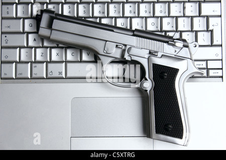 a silver gun on a Macbook pro laptop , conceptual image , metaphor Stock Photo