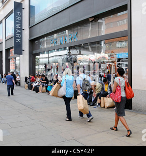 Shoppers with brown paper shopping bags walking past or sitting on window sill Primark clothing shop Oxford Street scene London West End England UK Stock Photo