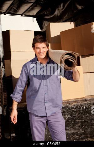 A portrait of a professional mover with a carpet and boxes in the background Stock Photo