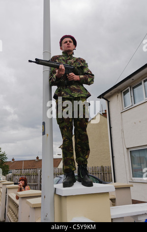 Youth dressed as a British Soldier from the Parachute Regiment holds a rifle while standing on a wall. Stock Photo