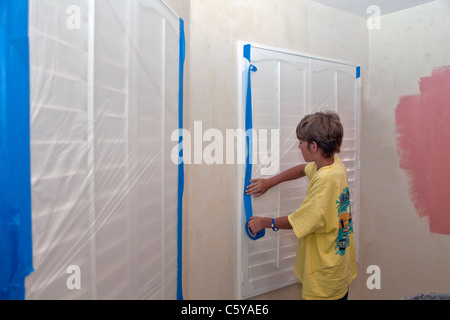 11 year years old caucasian boy using painter's tape to protect windows with plastic sheeting. MR © Myrleen Pearson Stock Photo