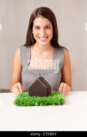 A woman holding a model house which is sitting on a turf of grass Stock Photo