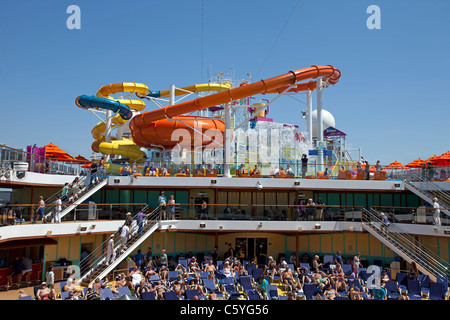 Water slide aboard a cruise ship in the Mediterranean Sea.  Vacationers and tourists relaxing in lounge chairs on the deck below Stock Photo