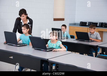 USA, Illinois, Metamora, Female teacher assisting children (8-9, 10-11) using laptops in computer lab Stock Photo