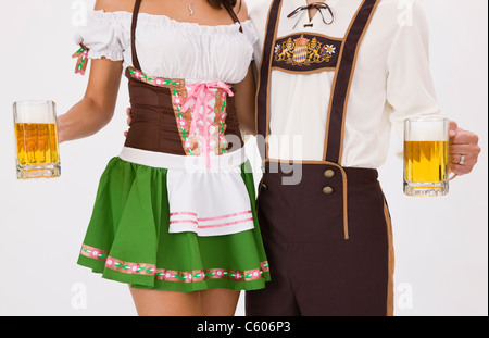 Young couple wearing Oktoberfest costume holding beer stein, studio shot Stock Photo