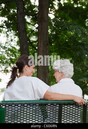 USA, Illinois, Metamora, Rear view of female nurse and senior woman sitting on park bench Stock Photo