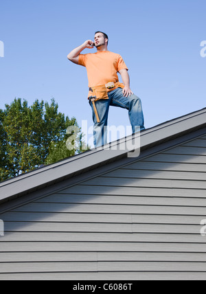 USA, Illinois, Metamora, Young worker standing on roof and talking via mobile phone Stock Photo