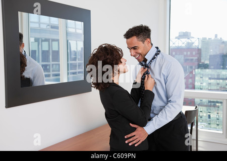 USA, New York, New York City, young woman helping smiling man tying tie in hotel room