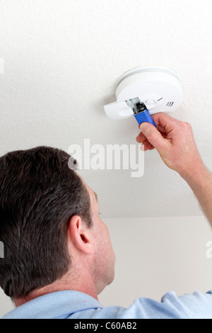 Man changing smoke alarm battery. Man carefully replacing 9 volt battery in round white ceiling smoke alarm detector for the safety of his household. Stock Photo