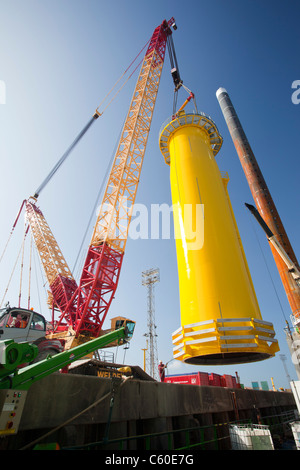 A crane lifts a transition piece of a wind turbine onto a jack up barge, ready to construct the Walney offshore wind farm Stock Photo