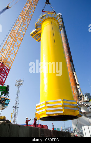 A crane lifts a transition piece of a wind turbine onto a jack up barge, ready to construct the Walney offshore wind farm Stock Photo