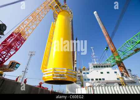 A crane lifts a transition piece of a wind turbine onto a jack up barge, ready to construct the Walney offshore wind farm Stock Photo