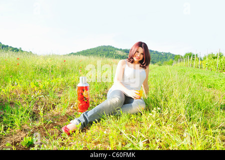 Woman drinking from thermos in field Stock Photo