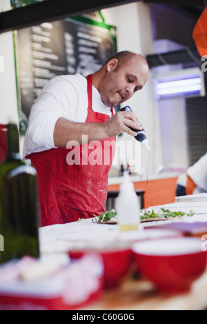 Chef drizzling oil over pizza in kitchen Stock Photo