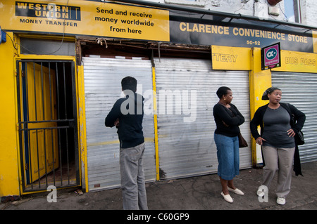 Hackney . Clarence Road, scene of last night's riot. Bystanders in the street in front of convenience store trashed by looters Stock Photo