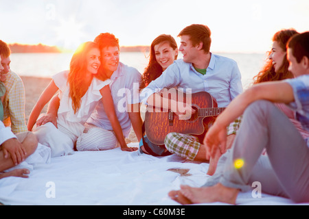 Man playing music for friends on beach Stock Photo