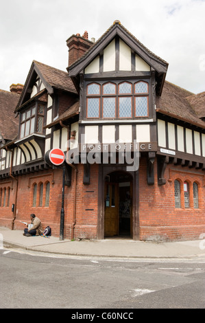 Arundel West Sussex the 19th century mock Tudor village post office with man selling The Big Issue sitting on the pavement street scene road sign Stock Photo