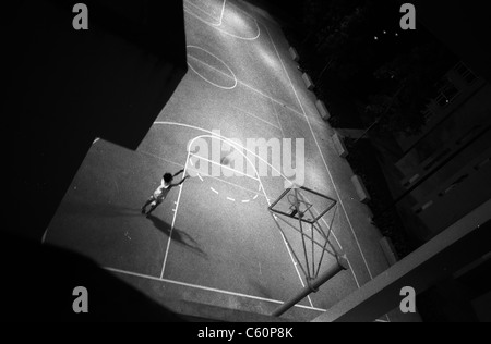 lone young man practicing basketball at night, singapore Stock Photo