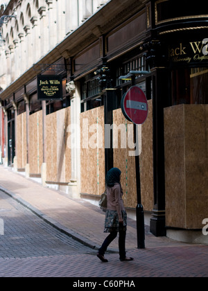 Young Muslim woman walks past a boarded-up Jack Wills store on New Street Birmingham following the riots of 2011. Stock Photo