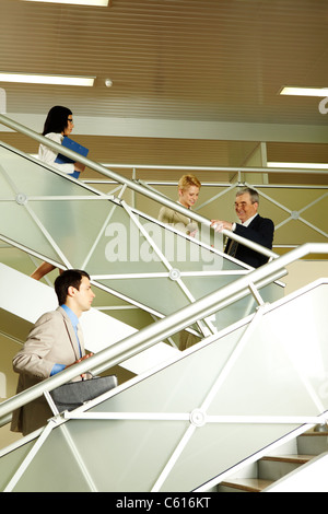 Photo of busy partners communicating while going upstairs in office building Stock Photo