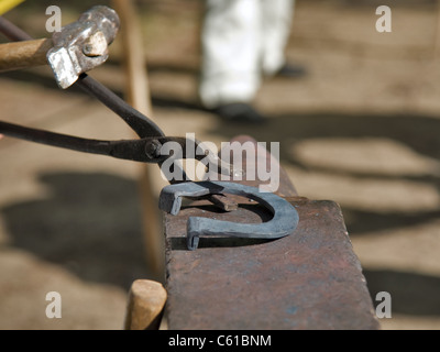 hands of blacksmith by working metal with hammer and anvil. Hammering glowing steel - to strike while the iron is hot. Stock Photo