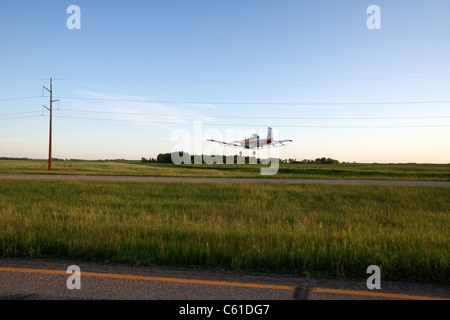 small cessna a118b cropdusting aircraft flying low over highway and dusting crop fields under electricity wires north dakota usa Stock Photo