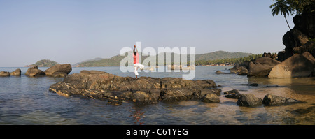 An Indian man does yoga on the rocks of the bay at at the popular tourist resort destination of Palolem Beach, Goa state, India Stock Photo