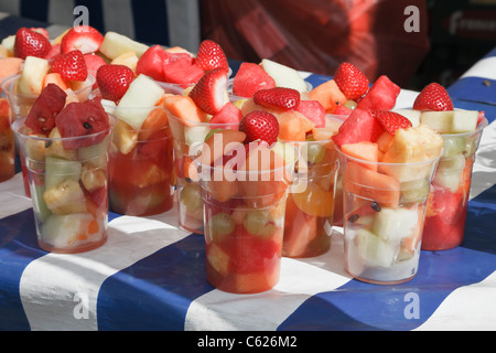 Mixed fresh fruit cocktails for sale in disposable plastic cups on a market stall with blue and white tablecloth in summer Stock Photo