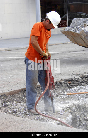 A construction worker wearing a safety helmet stands using a jackhammer to remove old cement at a building project Stock Photo