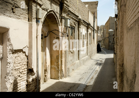 A woman wearing a black chador walks down a traditional narrow brick alleyway in the historic old city district of Tehran Iran. Stock Photo
