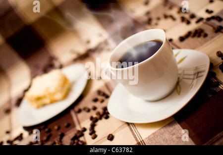 Very hot coffee in cup and cake on table, cake in blurred background Stock Photo