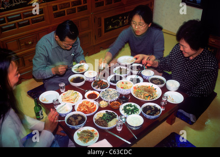 Family sitting at dinner table eating variety of home made Korean foods in South Korea