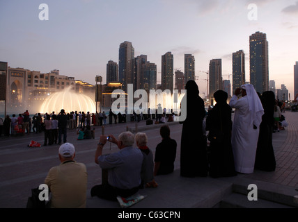 Spectators watching the water and light display of the Dubai Fountain on Burj Khalifa Lake at dusk in Dubai, Stock Photo
