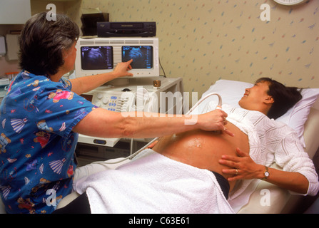 Female doctor giving ultrasound test to pregnant woman between 5-7months pointing at fetus on monitor screens Stock Photo