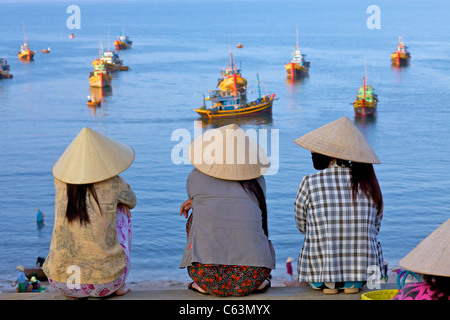 Three Vietnamese women watching fishing boats off coast of Mui Ne,  Vietnam Stock Photo