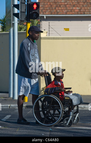 Boy in a wheelchair is assisted to cross a road in Cape Town South Africa Stock Photo