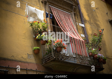 Typical old balcony with curtains, colored flowers and shirt drying on windows - Sicily, Italy. Stock Photo