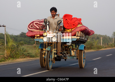 Indian motor tricycle at sunset carrying cargo up a highway in West Bengal India Stock Photo