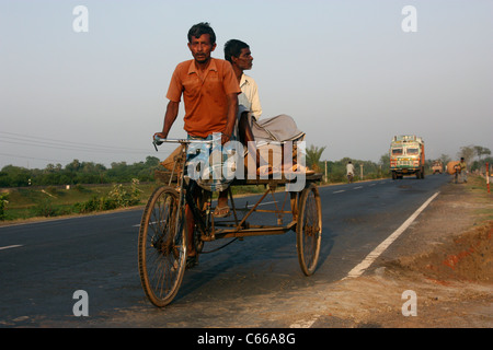 Indian pedal tricycle at sunset carrying cargo and passenger up a highway in West Bengal India Stock Photo