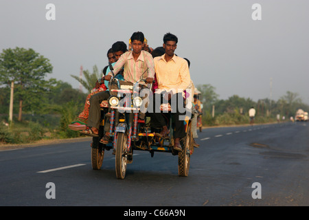 Heavily loaded Indian tricycle motor rickshaw carrying passenger up a highway at sunset in West Bengal India Stock Photo