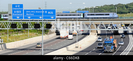 Transport concept choices passenger train on railway bridge crossing road traffic Junction 28 of the M25 motorway large blue gantry signs Brentwood UK Stock Photo